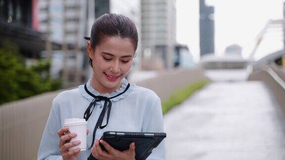 年轻的亚洲成年女性拿着电子平板电脑喝着咖啡上班商务人士去上班