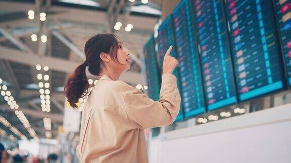 快乐的亚洲女旅客在机场候机楼查看航班时刻表旅游旅程旅行概念