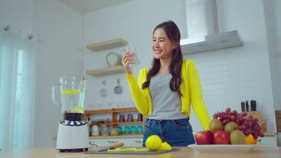 年轻的亚洲女子微笑着在厨房喝维他命水