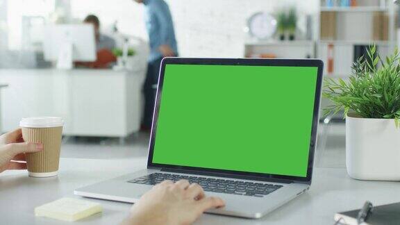 一个男人的手在笔记本电脑的绿色屏幕上工作的特写在背景模糊和明亮的办公室里一个人靠近另一个人他们在讨论