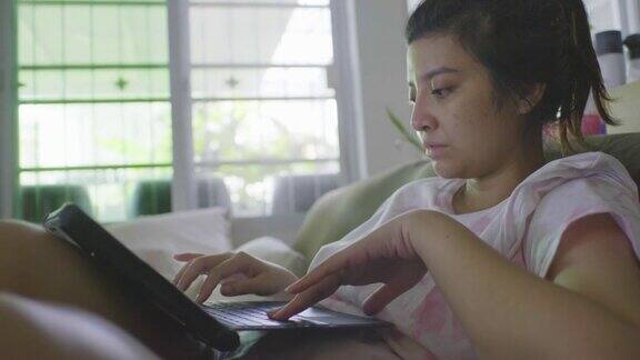 亚洲商务女性穿着休闲装在家里客厅的沙发上使用笔记本电脑工作