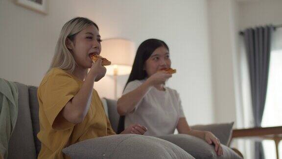 两个朋友的微笑漂亮的女人看电视和吃披萨在家里的客厅