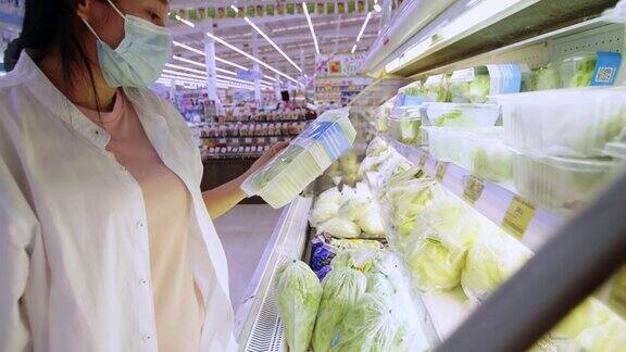 新常态保持社交距离亚洲女性戴着防护口罩在超市选购蔬菜新冠肺炎疫情爆发后女性在超市推着购物车购物