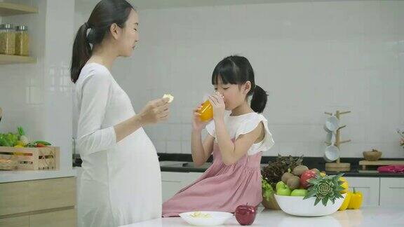 微笑的怀孕母亲和女儿享受在厨房一起