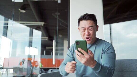 快乐快乐的亚洲男子自由职业者、雇员、工人庆祝手机获胜兴奋万分的幸运儿在短信中收到好消息使用智能手机
