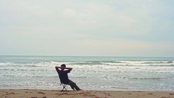 亚洲人以波浪的慢动作为活动概念坐在以大海为背景的沙滩上的小椅子上放松