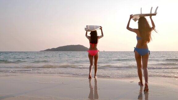 两个美丽的性感的年轻女子冲浪女孩在比基尼与冲浪板在海滩日落或日出假期iStock