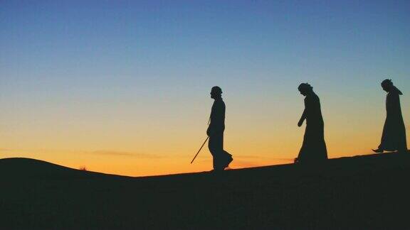 阿拉伯人在沙丘上行走的剪影