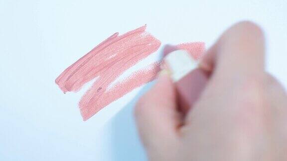女用手在白色背景的特写上涂抹粉色口红