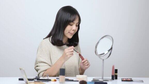 年轻的亚洲女性用口红化妆美丽的女人看着镜子和化妆
