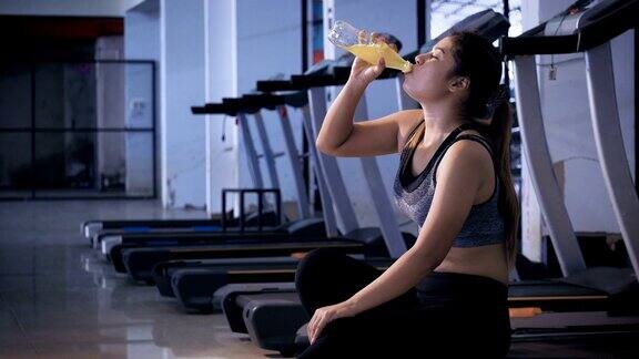 年轻的亚洲运动女性在健身房喝一瓶矿泉水的肖像