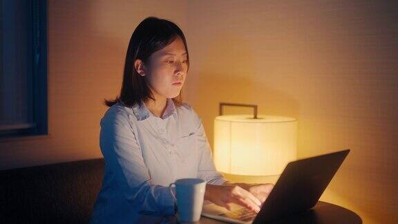 年轻的女商人在出差期间在酒店房间里用笔记本电脑工作到深夜