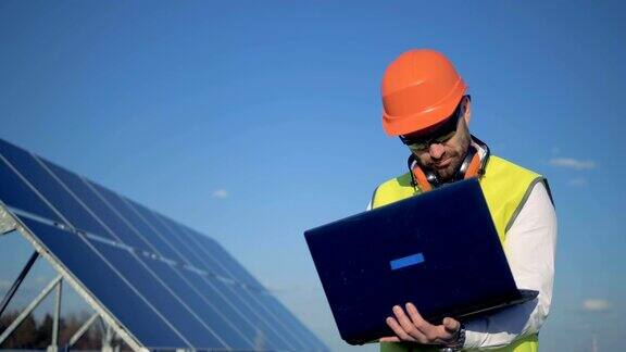 一个工人站在大楼的太阳能板旁边在他的笔记本电脑上打字4k