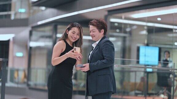 2名中国女性白领在会议室外看着智能手机