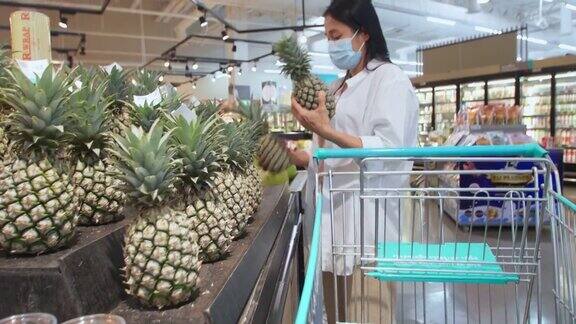 新常态保持社交距离亚洲女性戴着防护口罩在超市选购水果新冠肺炎疫情爆发后女性在超市买水果