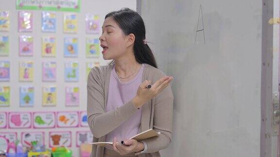 年轻的亚裔女老师在学校的白板上写字在学校的课堂上教学生