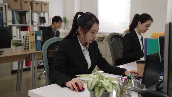 中国女员工穿着西装聚精会神地使用笔记本电脑与其他同事作为一个团队在办公室工作