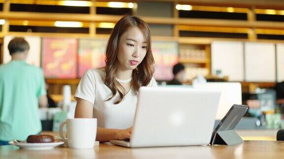 年轻的成年人快乐微笑的亚洲学生在线学习在网上聊天在网上聊天会议使用笔记本电脑在咖啡馆或办公室大学学院女生远程学习