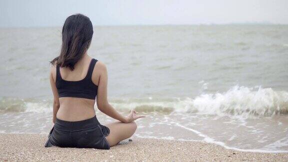 年轻的亚洲女子在海滩上练习瑜伽4k的决议