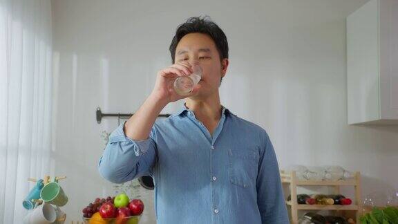 画像的亚洲有吸引力的男性喝一杯水在厨房年轻口渴的英俊男子拿着杯子喝清洁的天然矿物在清晨醒来后在家里保健