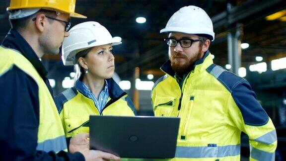 男性和女性工业工程师在使用笔记本电脑时与工厂工人交谈他们在重工业制造工厂工作