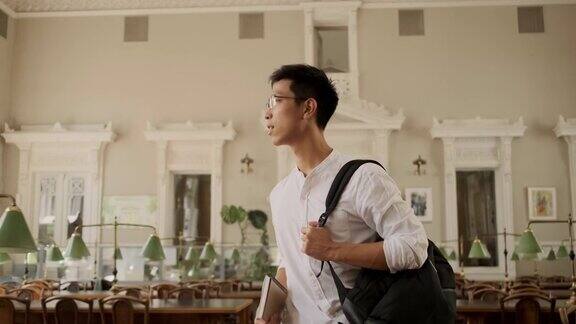 年轻的亚洲男学生微笑着梦游般地走过大学图书馆