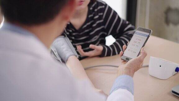 危险健康的年轻女性高血压病通过手机app检查医生在智能手机屏幕上检查病人的血压水平进行测量越过医生的肩膀查看