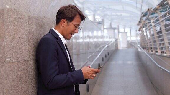 亚洲商人在办公大楼外用手机应用发短信