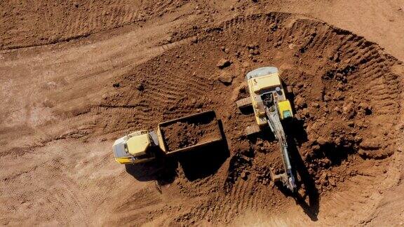建造道路交汇处黄色挖掘机铲斗将沙子装入自卸车车身从高处俯瞰