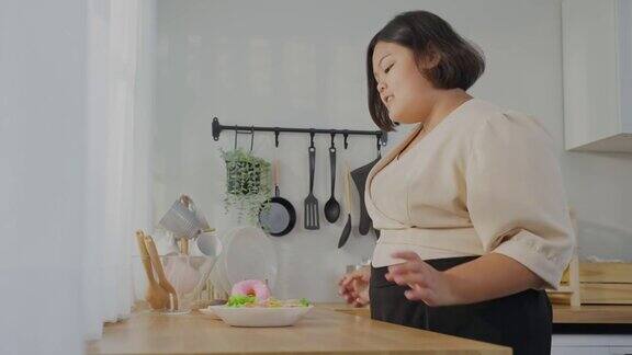 亚洲年轻的胖女人为盘子里的不健康食物感到高兴诱人的大码胖女孩走进厨房渴望选择甜甜甜圈而不是蔬菜沙拉在家里的桌子上