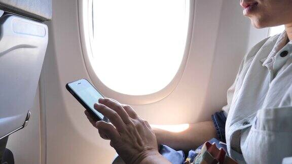 在飞行中坐在飞机窗口附近使用手机的女游客