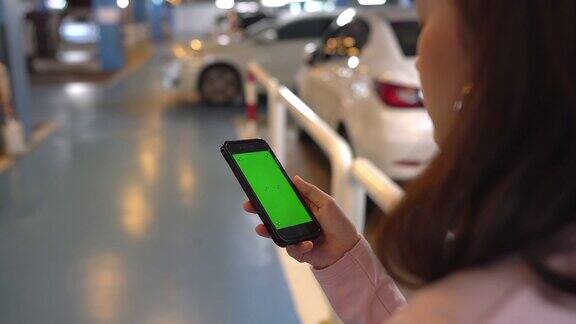 女人手持智能手机看绿色屏幕色度键显示在停车场使用手机通过滚动、滑动、手指来触摸屏幕