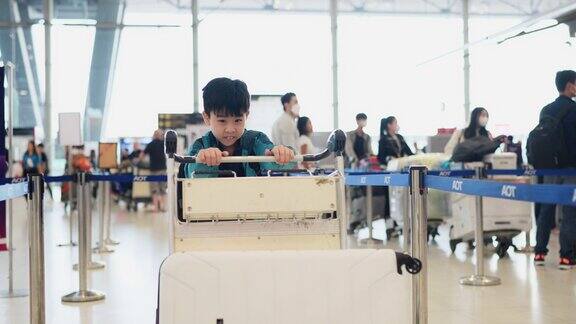 旅行是一种永无止境的学习经历穿着休闲夹克的亚洲男孩推着行李车在机场柜台排队办理登机手续在学校假期和家人一起旅行