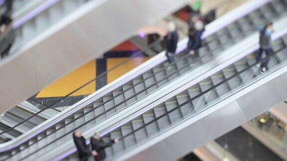 在现代化的购物中心里人们在自动扶梯上走动倾斜移位镜头拍摄超浅景深