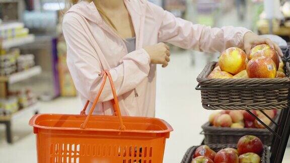 一名亚洲妇女在超市货架上摘苹果并闻了闻