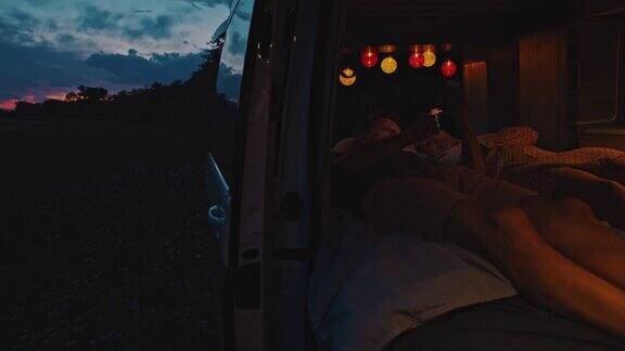 黄昏时分一对WS夫妇躺在他们的露营车里使用智能手机