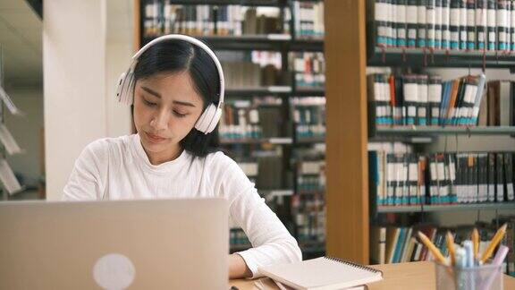 亚洲大学生十几岁的女孩在图书馆里用笔记本电脑读书为课程做在线研究为论文作业做笔记在线教育电子学习概念