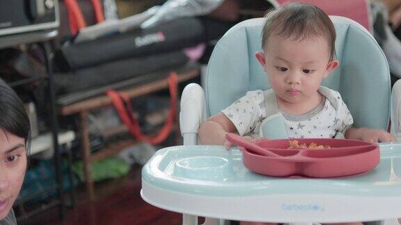真实的照片可爱的亚洲新生儿和妈妈坐在高脚椅上吃饭