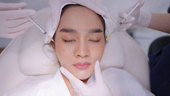 亚洲年轻漂亮的女性穿着浴袍裹着毛巾头巾躺在医生面前对额头和脸部皮肤进行面部年轻化注射亚洲年轻美丽的女性填充皱纹由A型肉毒杆菌毒素在脸上