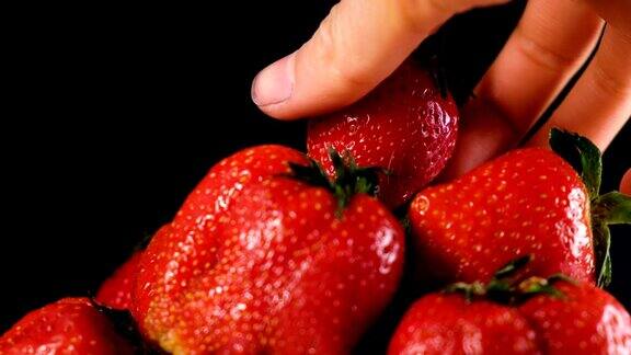 在黑暗的背景上一名男子在一大堆草莓上拿了一个草莓