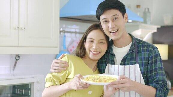描绘一对相爱的年轻夫妇在家里帮助做饭在浪漫的气氛中微笑着看着镜头