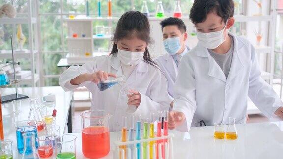 年轻的科学家女孩和男孩戴着卫生口罩喜欢在实验室里进行多彩的化学实验