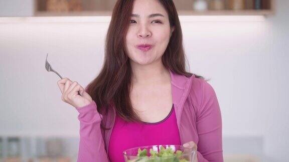 运动的年轻亚洲女性穿着运动服拿着沙拉碗在锻炼后吃健康的新鲜蔬菜沙拉保持减肥饮食和健康食品