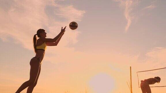 一个美丽的女人穿着比基尼与一个球在日落是准备做发球跳在沙滩上的沙滩排球比赛