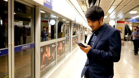 亚洲商人在火车站等车时用智能手机发短信