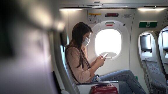 一名年轻女子戴着口罩坐在飞机座位上打电话