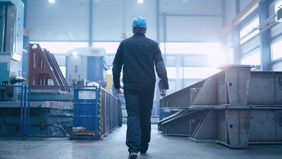 跟随镜头的工厂工人戴着安全帽走过工业设施