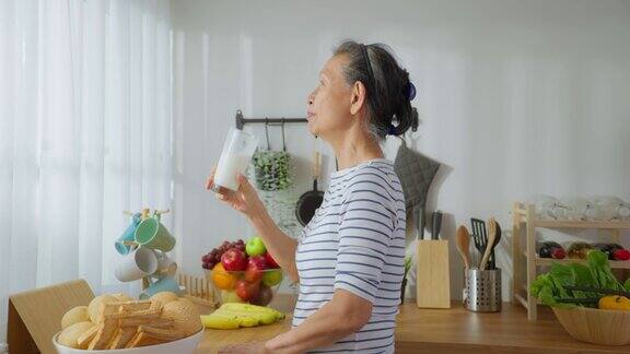亚洲高级成熟女性在家里的厨房喝一杯牛奶有魅力的老祖母抱着和喝着一杯牛奶早上醒来在家里的保健