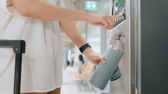 一名女子手持可重复使用的保温水瓶在机场装水