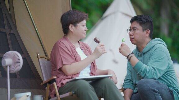 周末下午一对亚洲华人中年夫妇在露营帐篷前享受冰淇淋